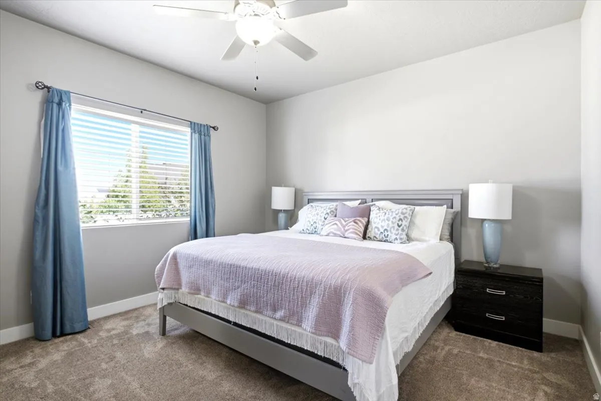 Carpeted room featuring a ceiling fan, a window with horizontal blinds, and a built-in headboard