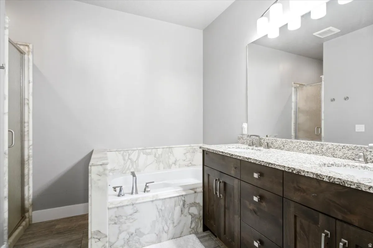 Soaking tub encased in white marble, dual sink vanity with stone countertop, dark wood-finish cabinetry, and a glass-enclosed shower