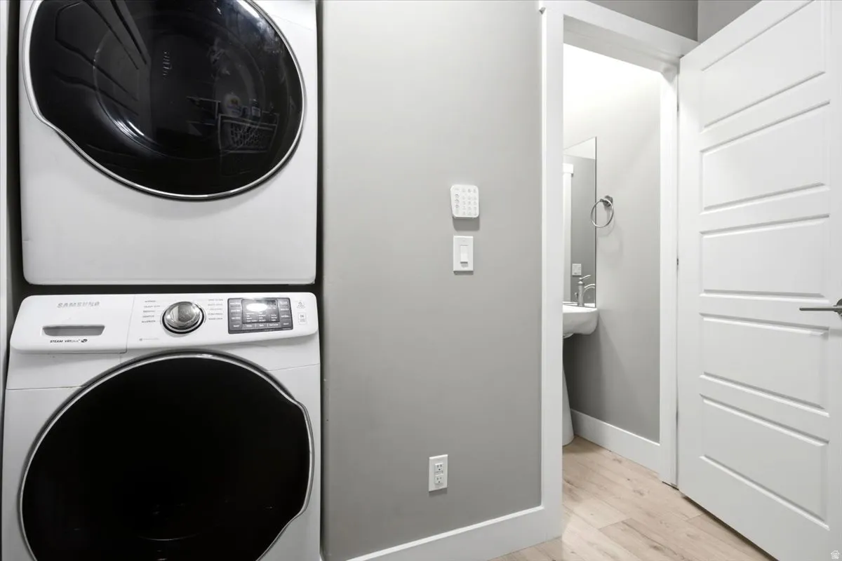 Dedicated laundry area featuring stacked front-load machines, light wood-finish flooring, and a white paneled door