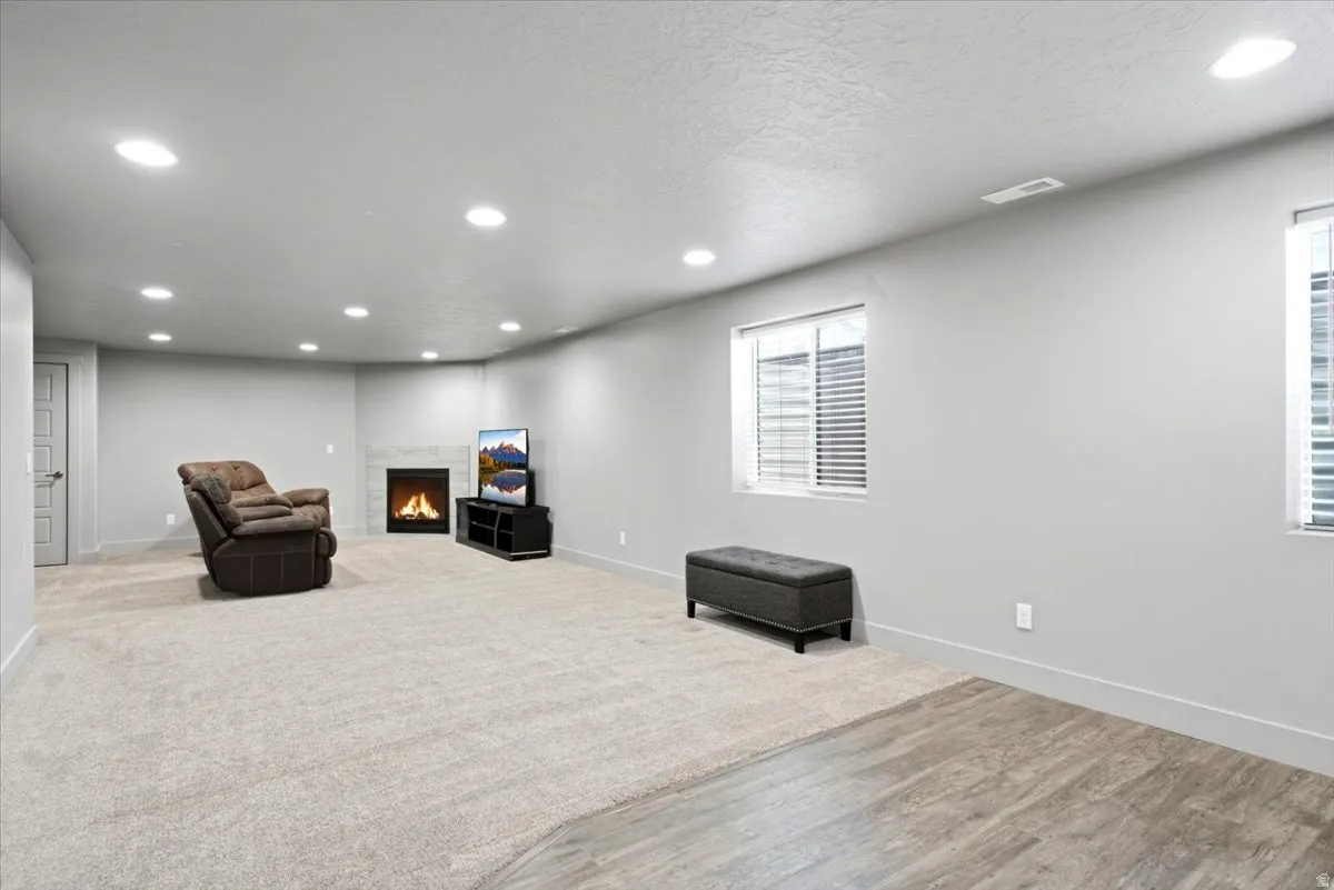 Spacious room featuring light-colored carpeting, recessed lighting, and a corner fireplace with a tiled surround