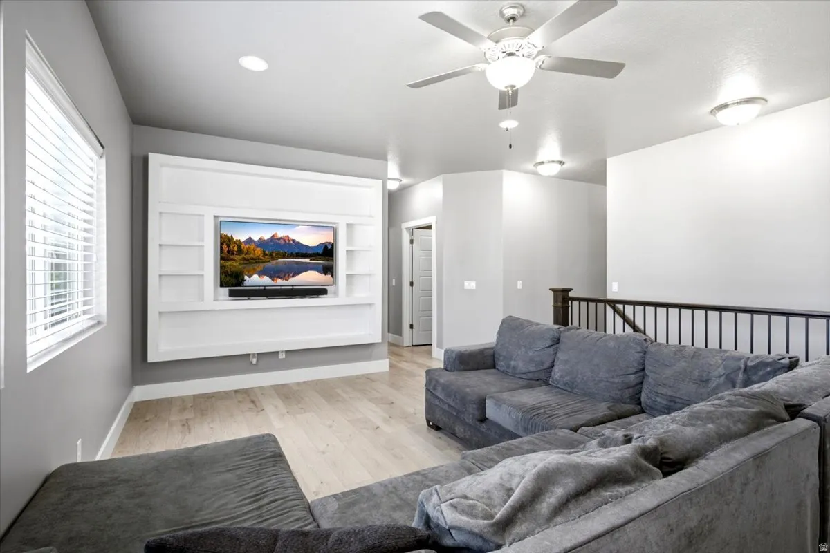 Living area featuring a custom white built-in media center with shelving, light wood-finish flooring, and a ceiling fan with integrated lighting