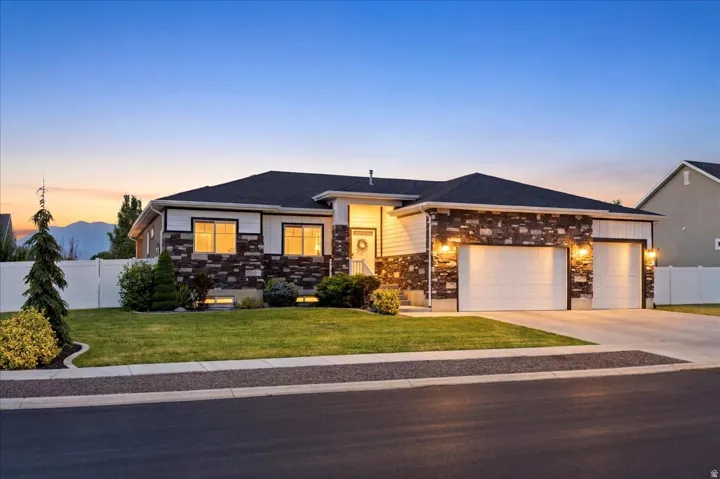 Contemporary facade with stone and siding accents, featuring a two-car garage, manicured lawn, and mature landscaping
