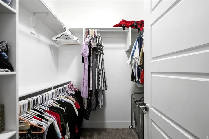 Walk-in closet featuring white built-in shelving, multiple hanging rods, and a paneled white door