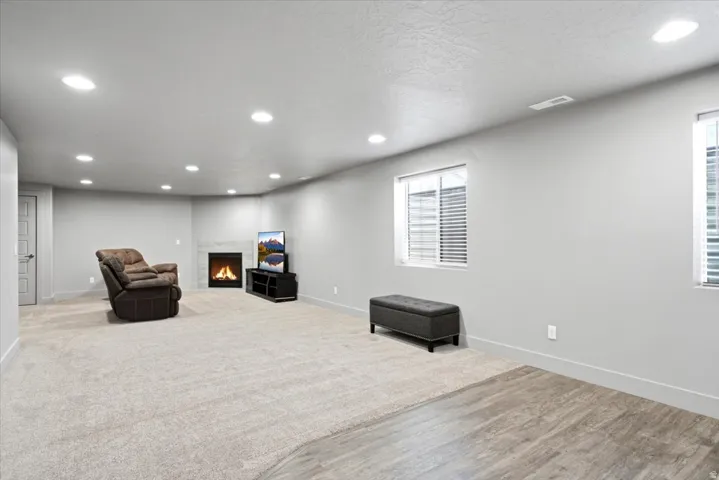 Spacious room featuring light-colored carpeting, recessed lighting, and a corner fireplace with a tiled surround