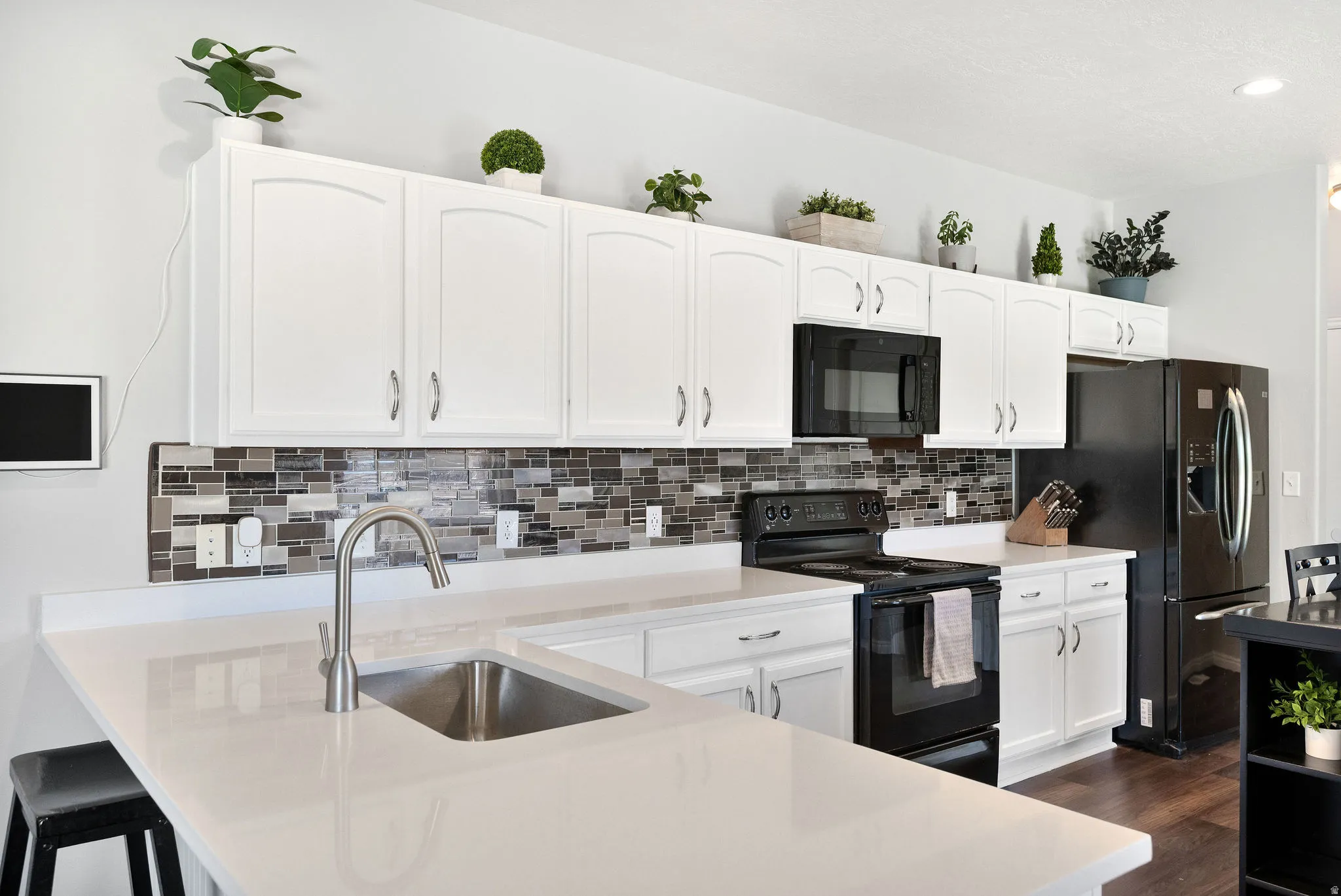 Modern kitchen featuring white cabinetry, light-toned countertops, a mosaic tile backsplash, and stainless steel sink with a gooseneck faucet