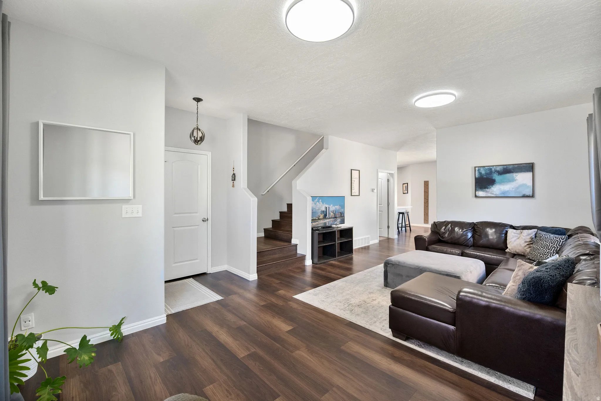 Spacious living area featuring wood-finish flooring, light gray wall tones, recessed lighting, a prominent entryway, and a visible staircase