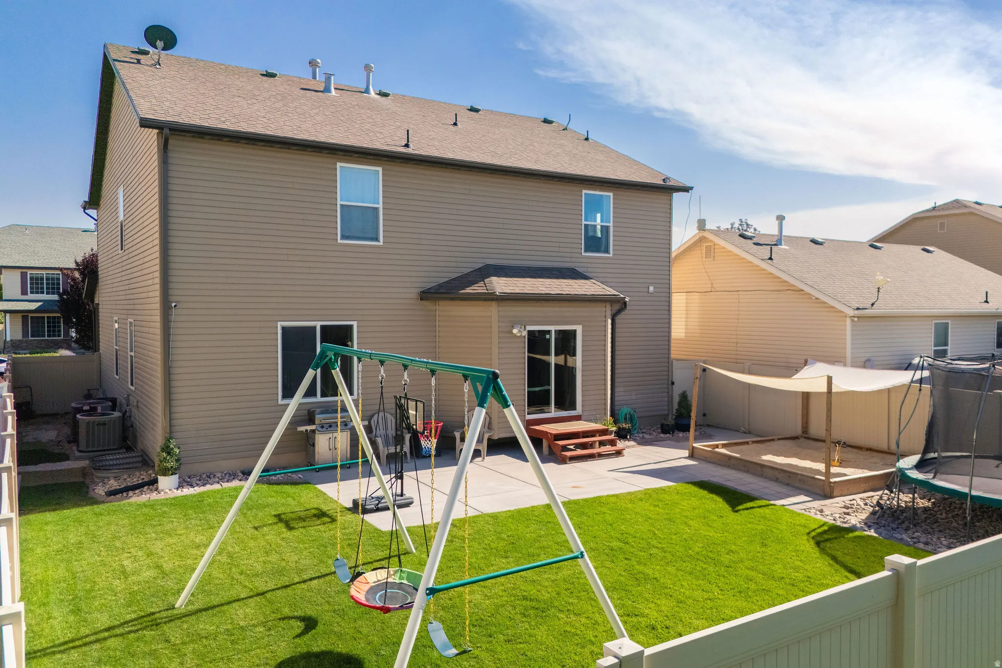 Expansive backyard featuring a manicured lawn, a large concrete patio, and a covered sandbox