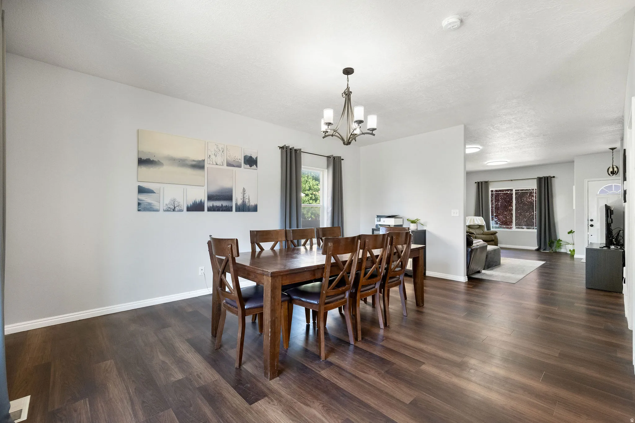Dining area featuring wood-finish flooring, a chandelier, light gray walls, and natural light from a window with drapes