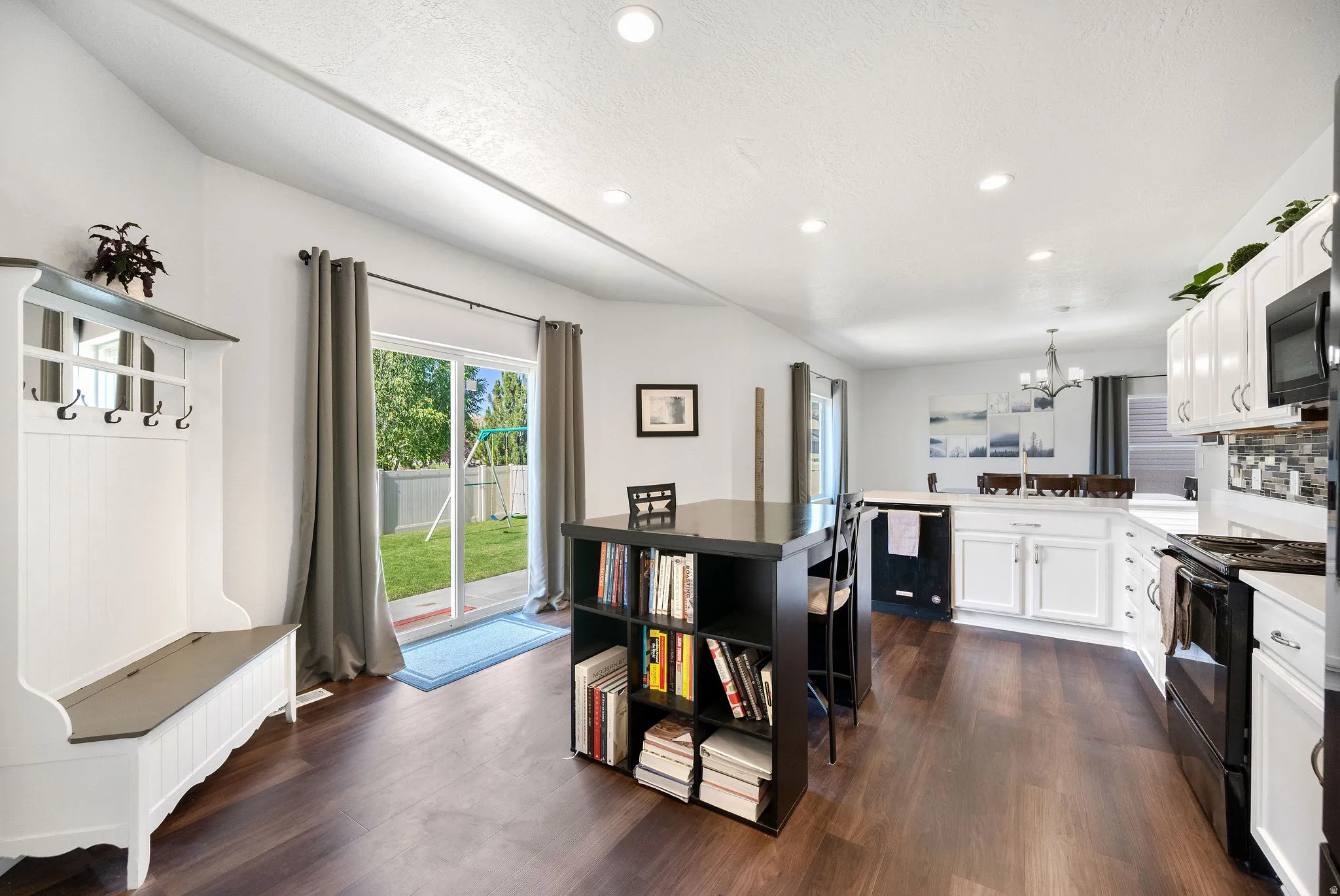 Open-concept kitchen and living area featuring dark wood-finish flooring, white cabinetry, a built-in kitchen island with shelving, recessed lighting, and a sliding glass door providing access to the backyard