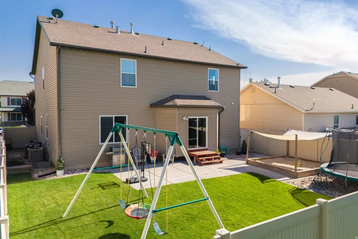 Expansive backyard featuring a manicured lawn, a large concrete patio, and a covered sandbox