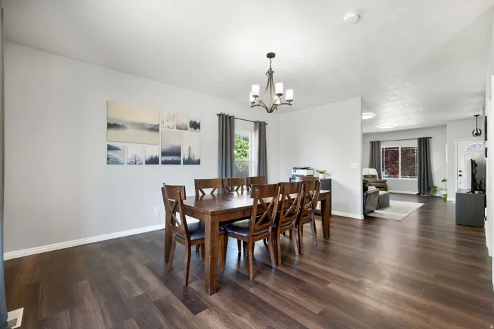 Dining area featuring wood-finish flooring, a chandelier, light gray walls, and natural light from a window with drapes