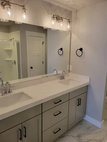 Dual vanity with light gray cabinetry, integrated sinks, chrome faucets, and white stone-finish countertops