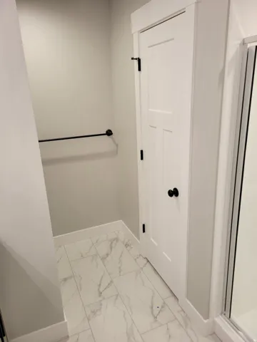 Bathroom featuring large format marble-look tile flooring, a white paneled door with matte black hardware, and a matte black towel bar