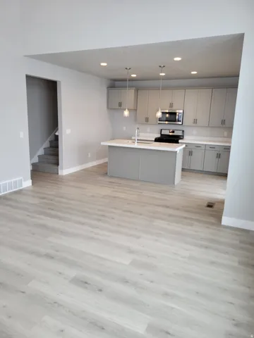 Open-concept layout featuring light wood-finish flooring, a contemporary kitchen island with a white countertop, gray cabinetry, recessed lighting, and stainless steel appliances