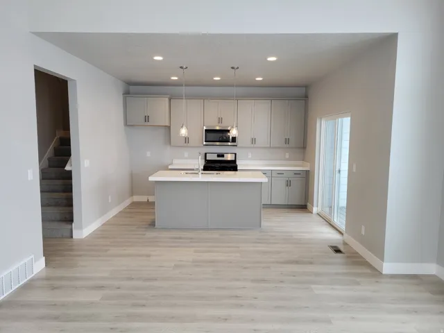Open-concept kitchen featuring an island with counter seating, light gray cabinetry, stainless steel appliances, and recessed lighting