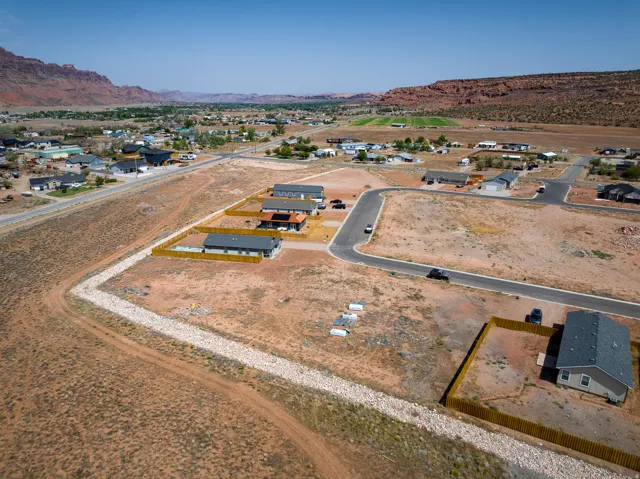 New construction homes featuring modern architectural styles, individual fencing, and paved roads, set against a backdrop of natural rock formations and distant greenery