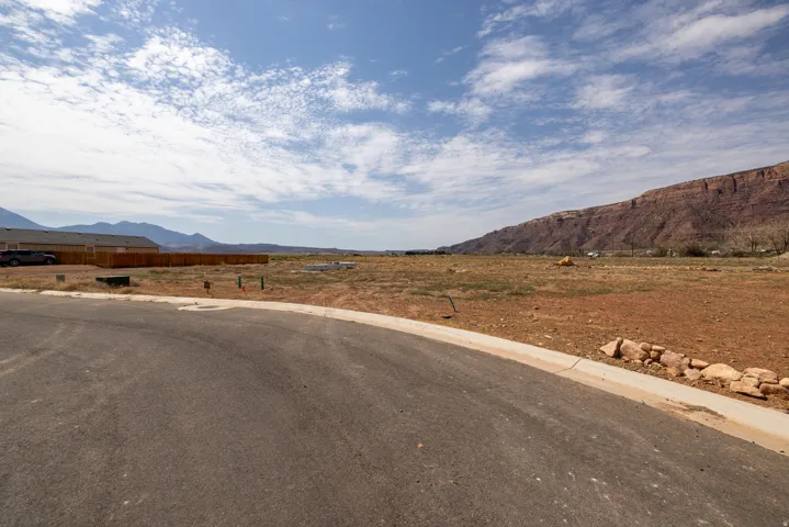 Expansive land parcel featuring existing paved road frontage, curb and gutter infrastructure, and mountain vistas