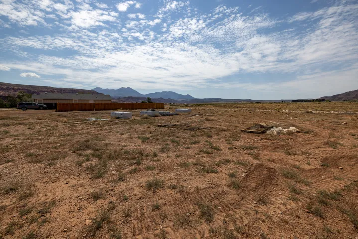Expansive open land with distant mountain ranges and a partially constructed building featuring a wood fence