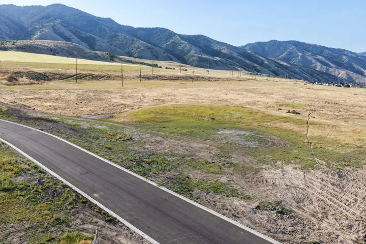Paved road frontage with defined curbing bordering expansive natural terrain, featuring distant mountain ranges and scattered utility poles