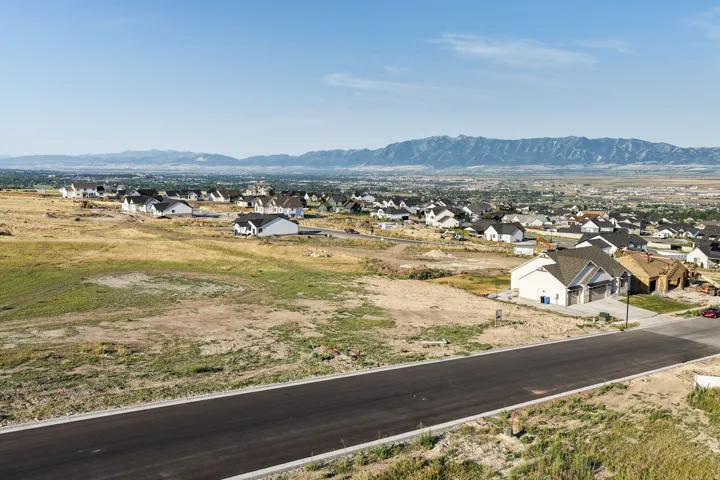Expansive landscape featuring distant mountains, open terrain, new residential construction, and a paved street
