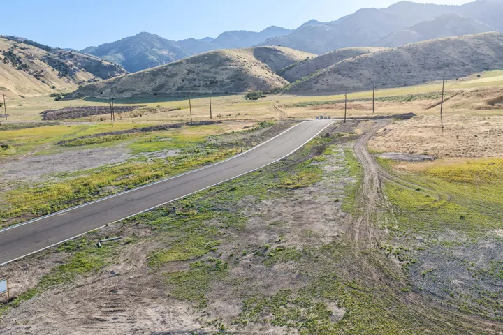Paved road with adjacent undeveloped land, featuring rolling hills and distant mountains