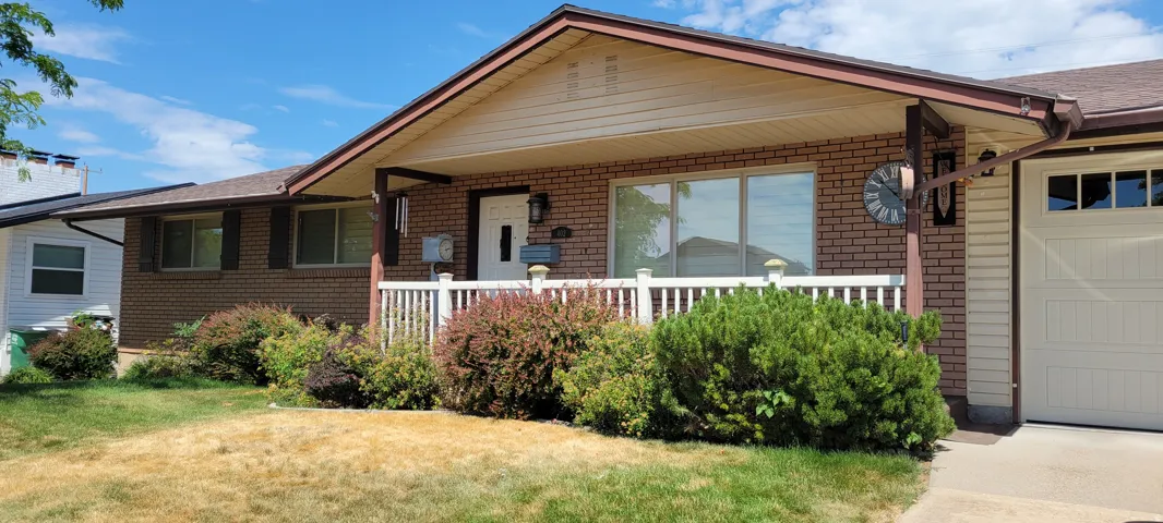 Brick facade home featuring a covered front porch with white railing, a beige garage door with upper window panels, and a gabled roofline