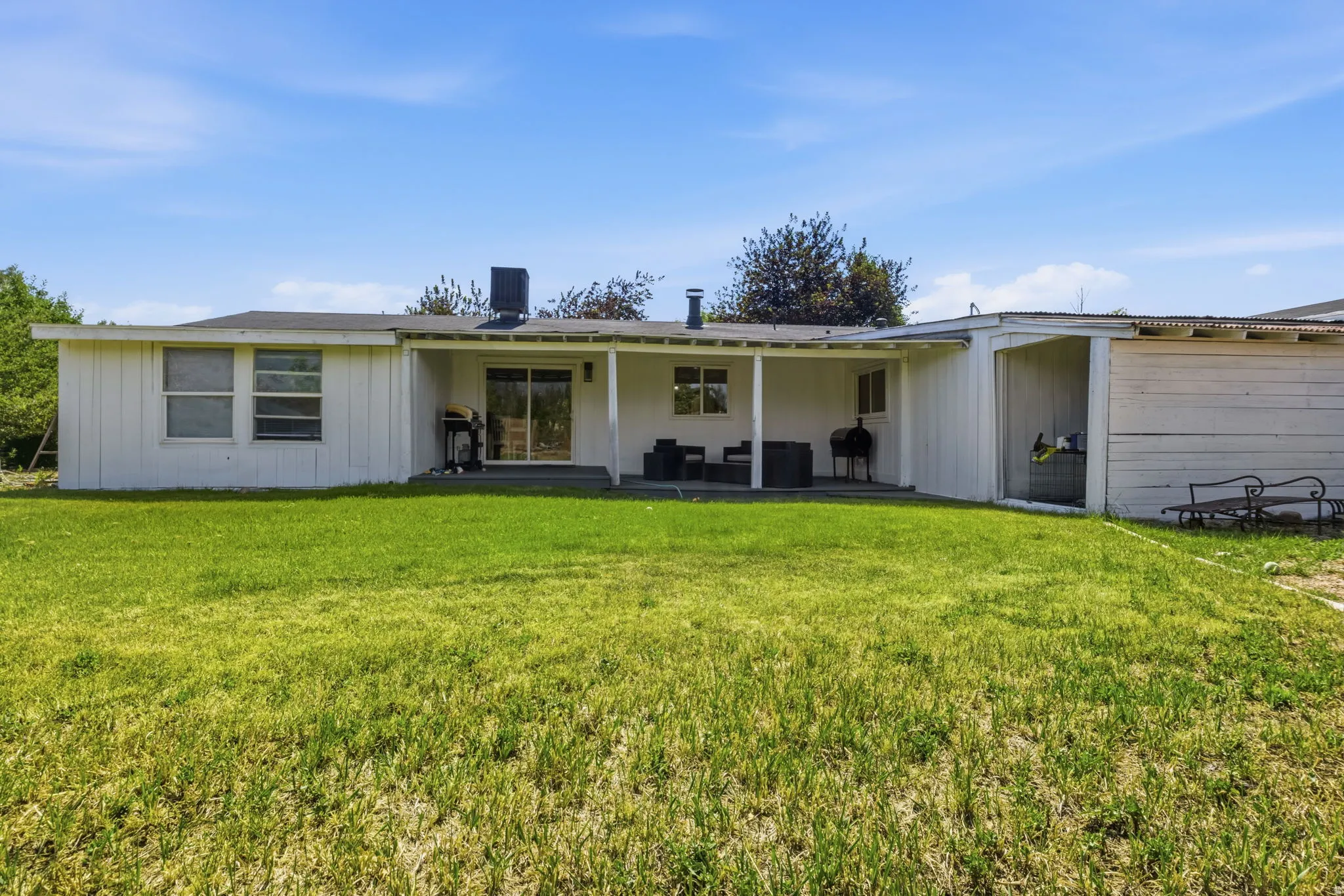 Expansive backyard featuring a covered patio, sliding glass door access, multiple windows, a storage shed, and a flat roofline