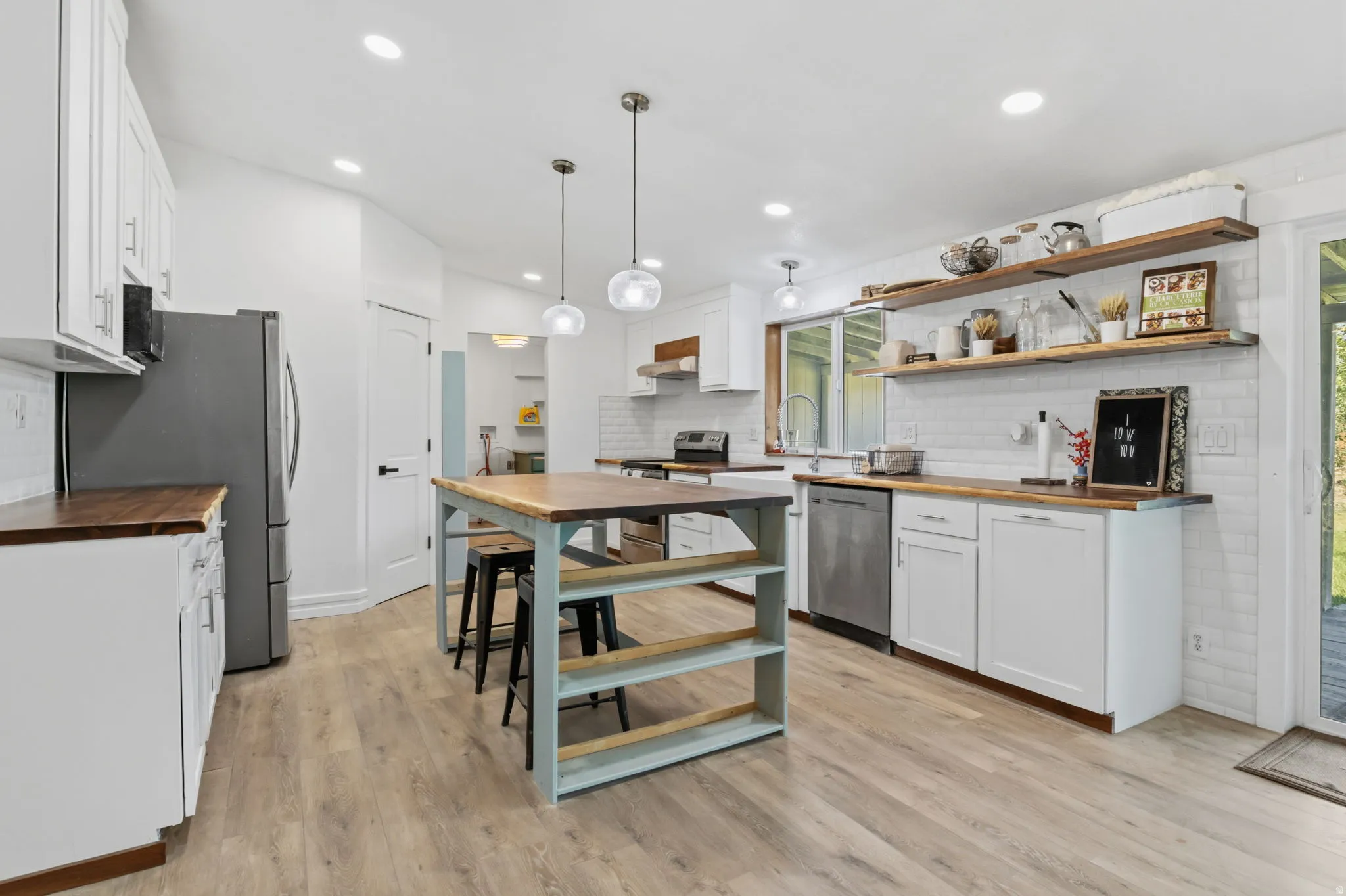 Open-concept kitchen featuring wood-finish flooring, white cabinetry, wood countertops, a central island with bar seating, and stainless steel appliances
