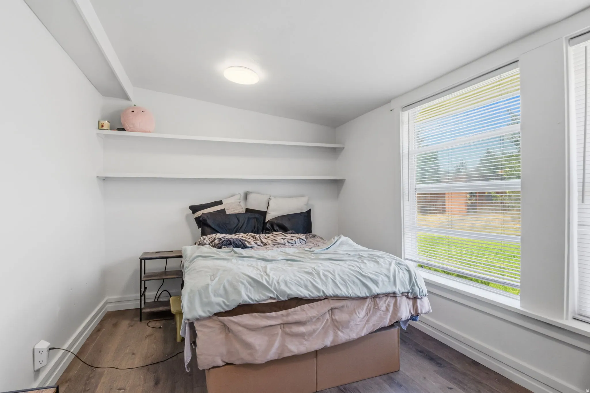 Compact room featuring wood-finish flooring, white walls, and a large window with horizontal blinds