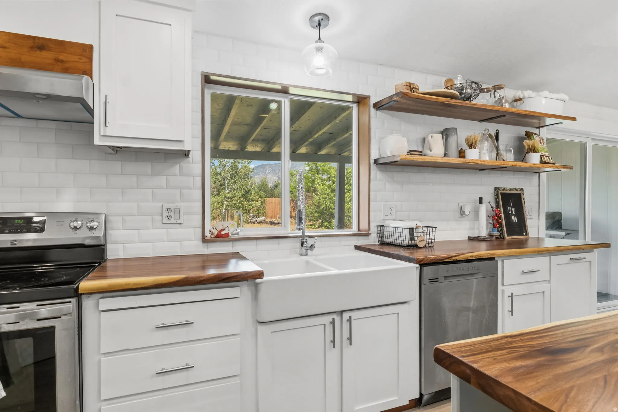 Kitchen featuring a double basin farmhouse sink, wood-finish countertops, stainless steel appliances, white subway tile backsplash, and open shelving