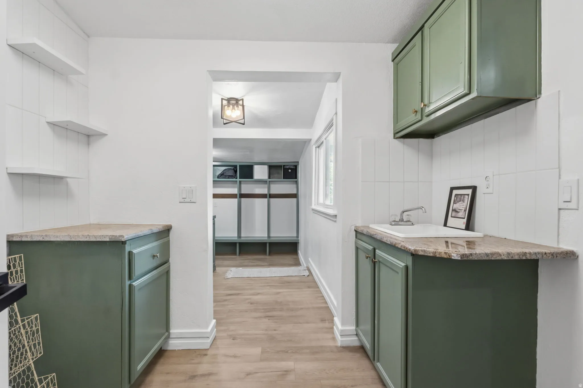 Kitchenette featuring sage green cabinetry, stone-look countertops, a built-in sink with faucet, white tiled backsplash, and wood-finish flooring