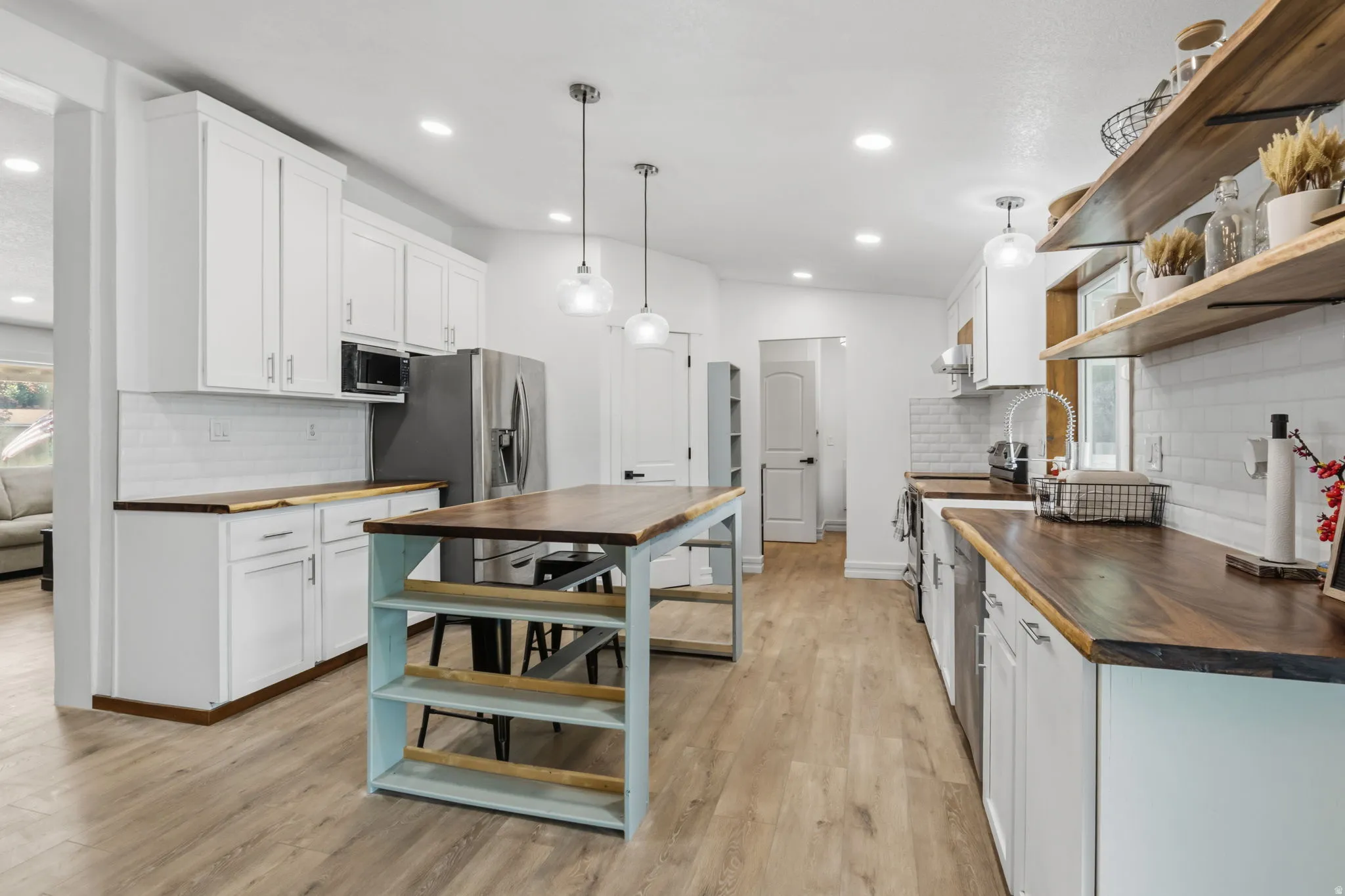 Open-concept kitchen featuring white cabinetry, wood-finish countertops, subway tile backsplash, and light wood-finish flooring