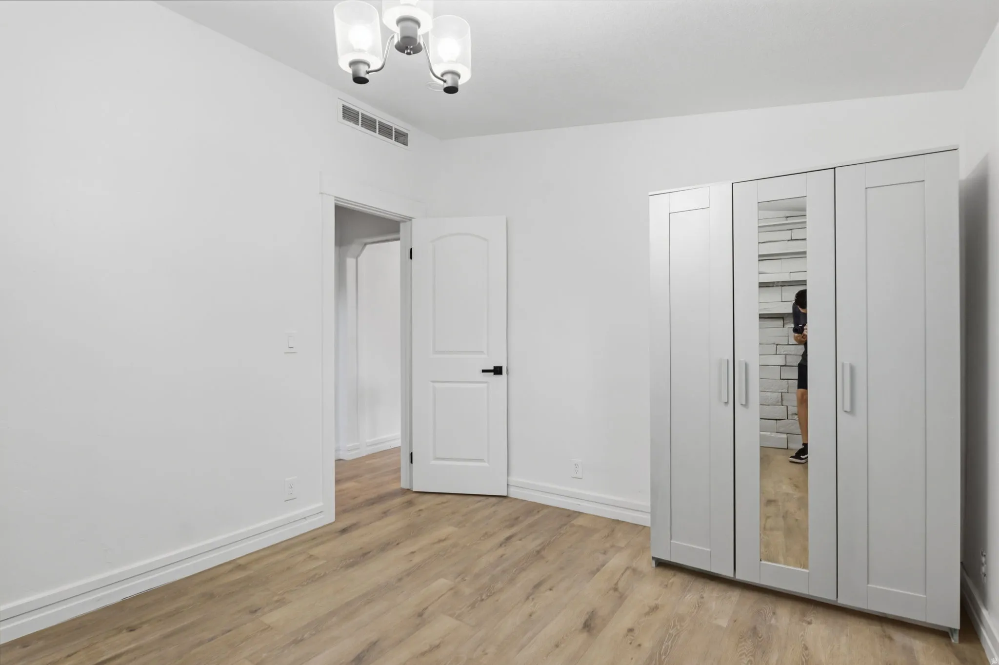 Room featuring light wood-finish flooring, white walls, and a modern ceiling light fixture