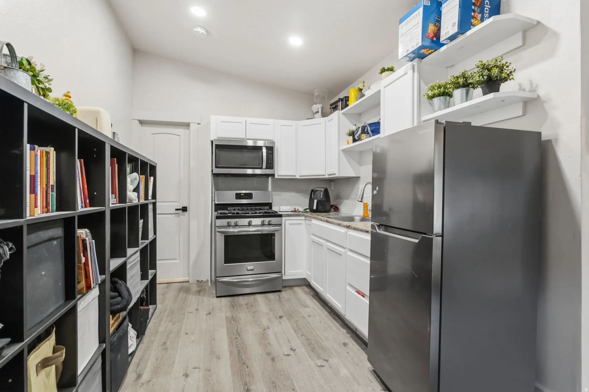 Kitchen featuring stainless steel appliances, white cabinetry, light-toned countertops, and wood-finish flooring