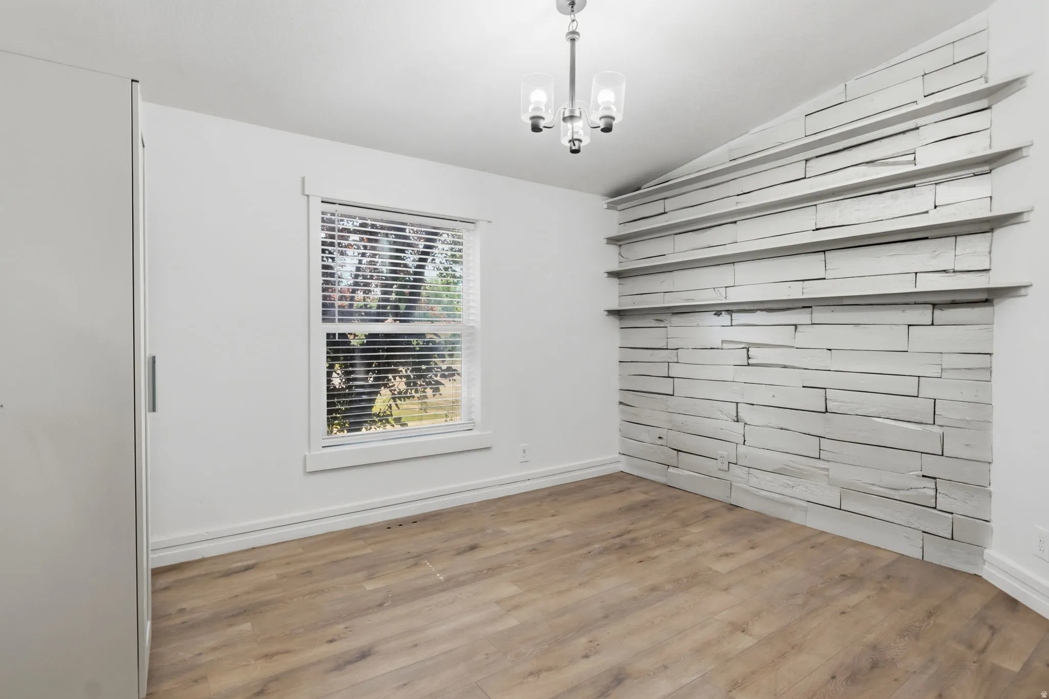 Interior room featuring a natural wood-finish flooring, a window with blinds, and a built-in wall treatment with shelving