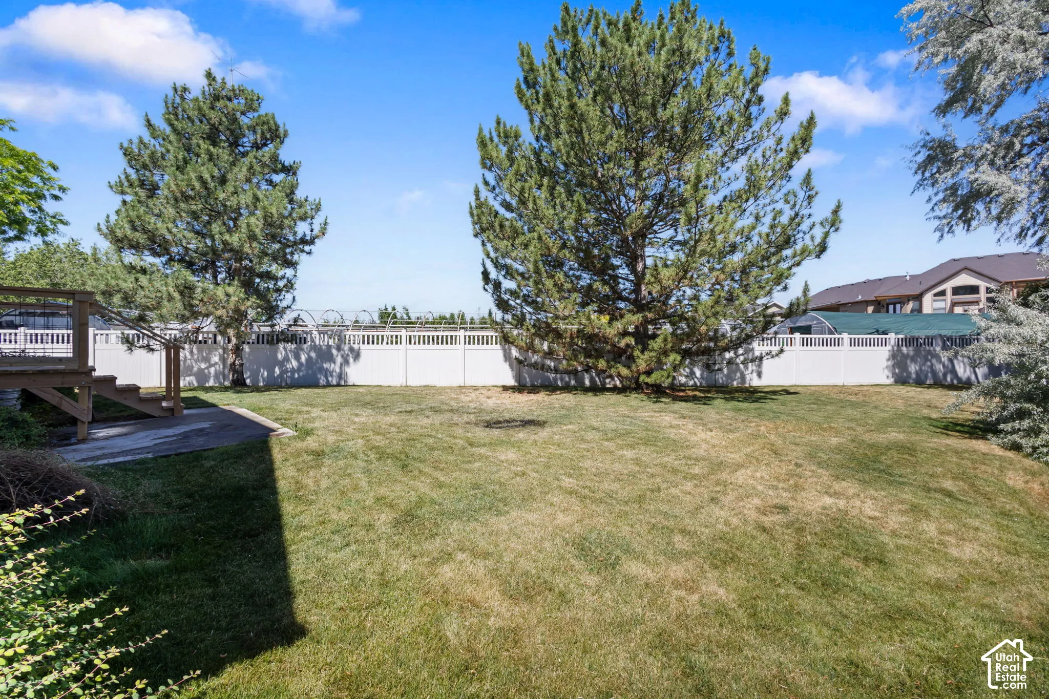 Expansive backyard featuring a leveled lawn, mature trees, white privacy fencing, and a wood deck with stairs