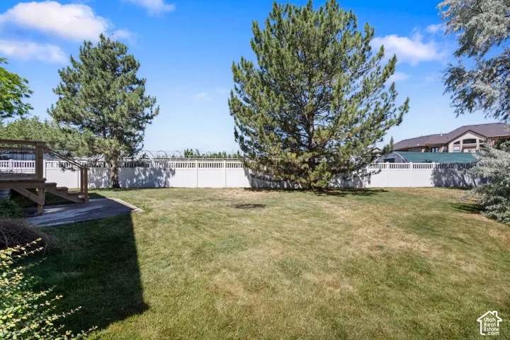 Expansive backyard featuring a leveled lawn, mature trees, white privacy fencing, and a wood deck with stairs