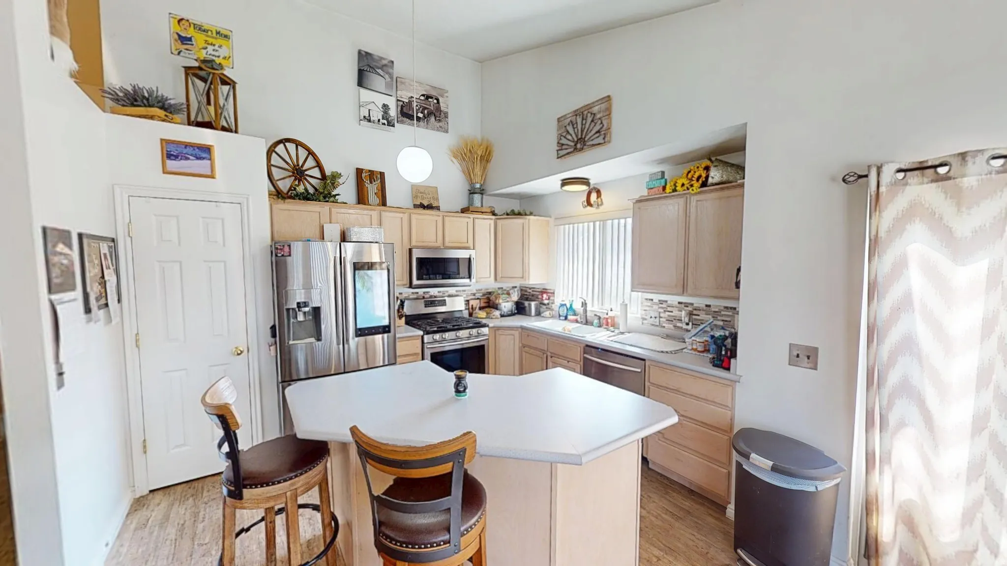Kitchen featuring wood-finish flooring, a central island with a light-toned countertop, light wood cabinetry, and stainless steel appliances