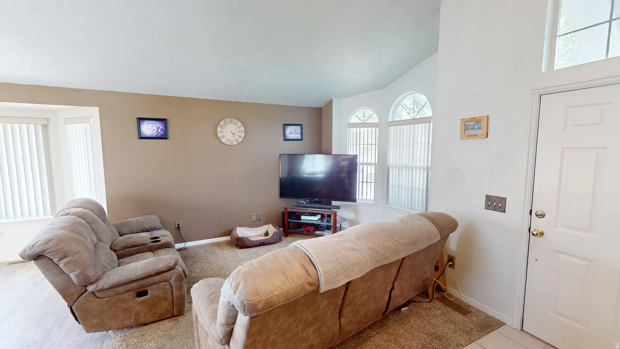 Living area featuring neutral-toned walls, high ceilings, arched windows with vertical blinds, and a paneled entry door