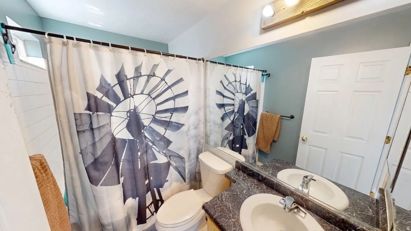 Bathroom featuring a dual vanity with undermount sinks, a large mirror, a toilet, and a shower with white subway tile