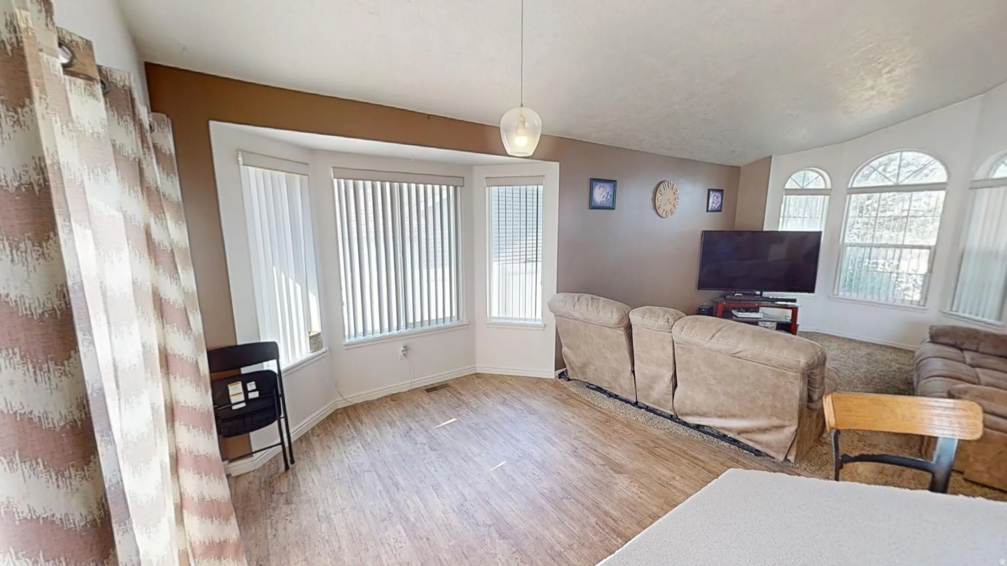 Living area featuring wood-finish flooring, a bay window with vertical blinds, and a suspended glass light fixture