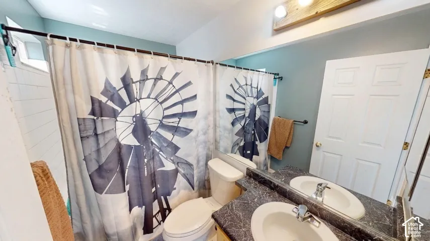 Bathroom featuring a dual vanity with undermount sinks, a large mirror, a toilet, and a shower with white subway tile