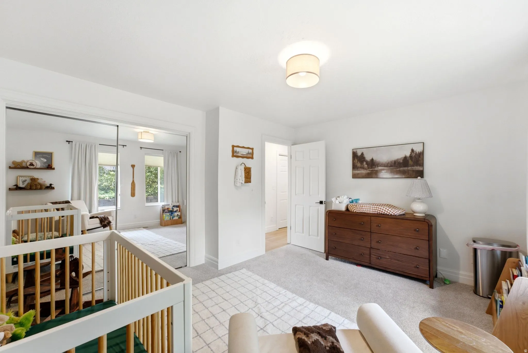 Bright room featuring white walls, light-colored carpet, a ceiling-mounted light fixture, and a white paneled door with dark hardware