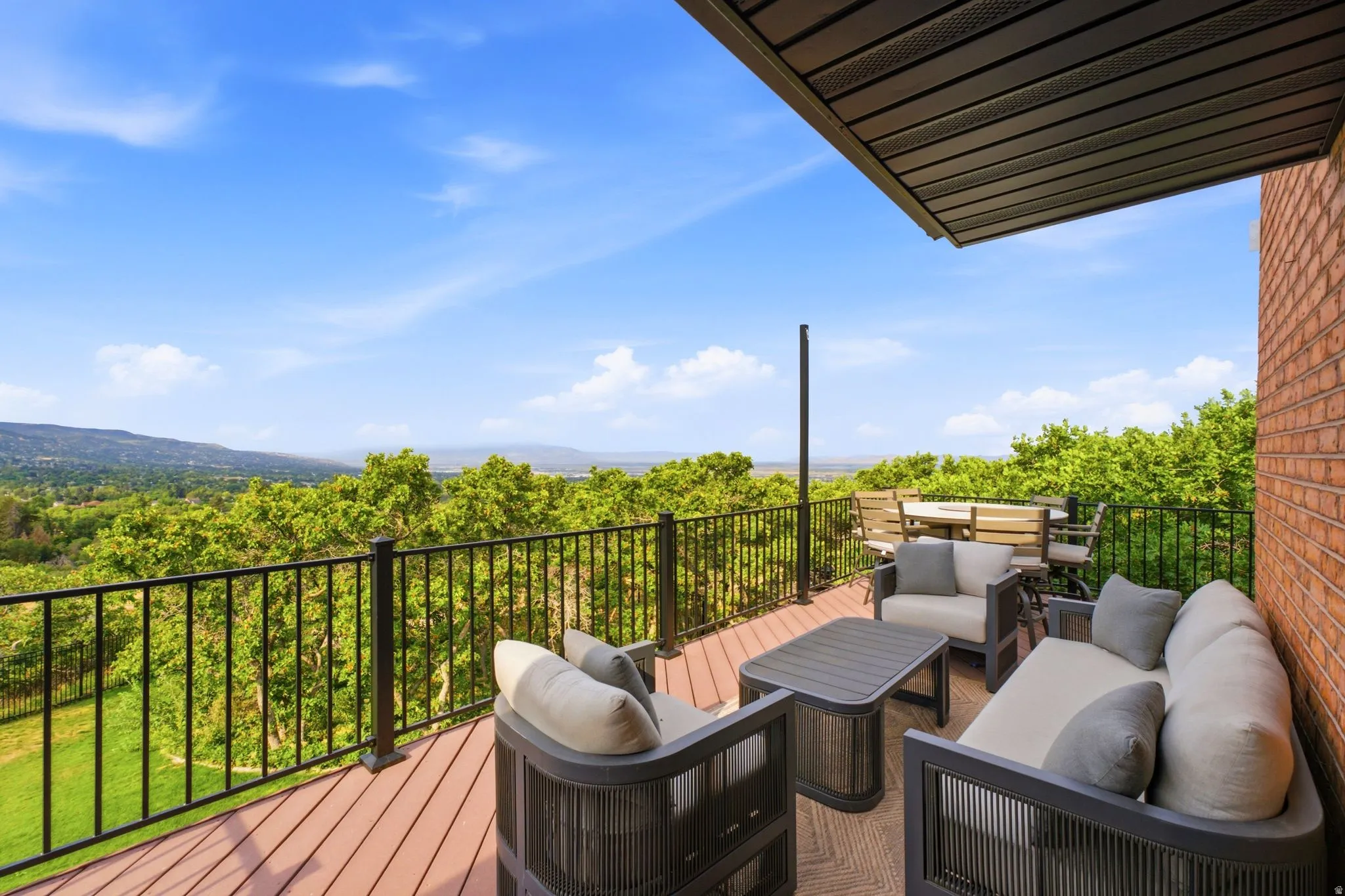 Elevated outdoor deck with composite wood-finish flooring, black metal railing, and a brick exterior wall