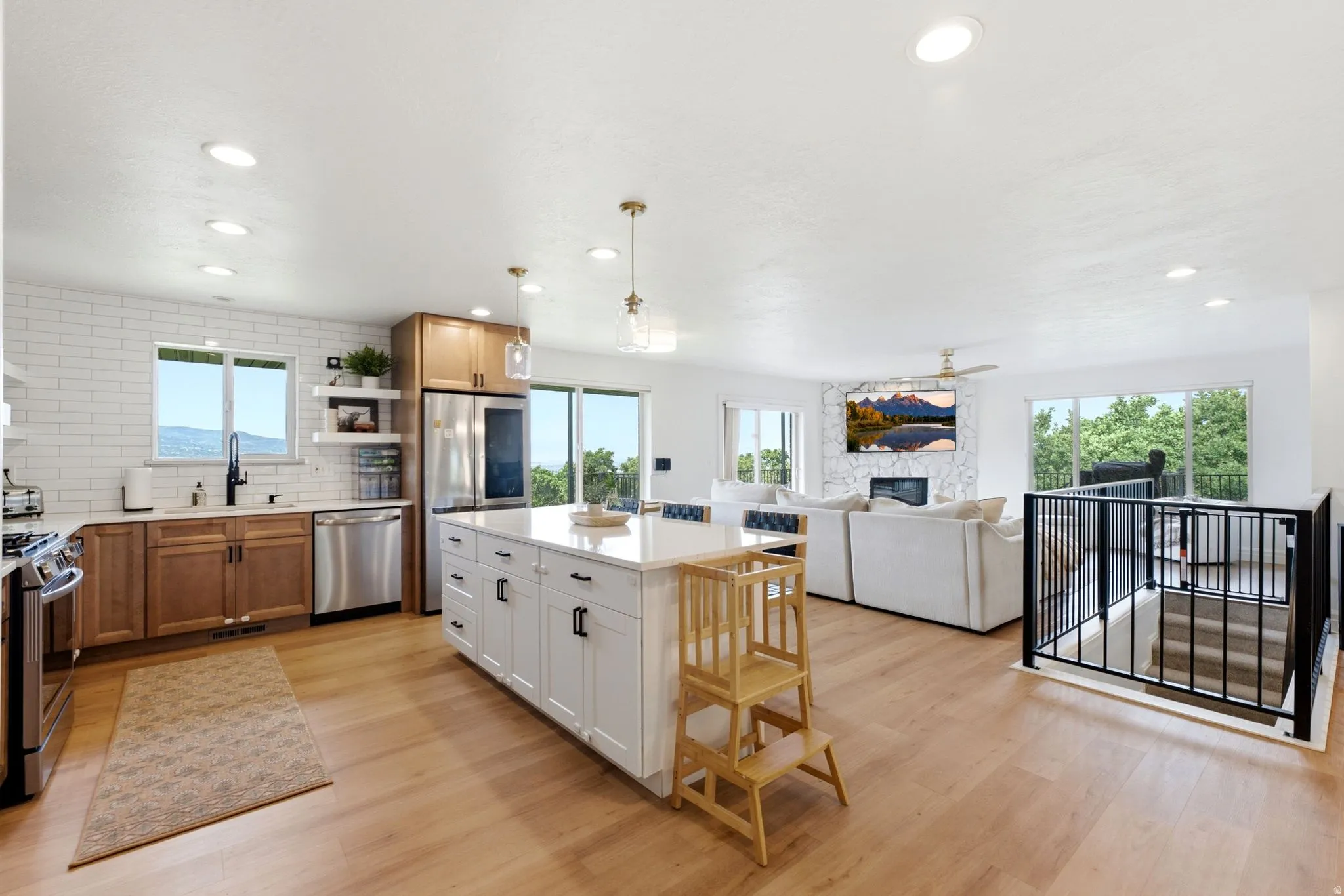 Open-concept living space featuring a kitchen with a white subway tile backsplash, stainless steel appliances, and a large central island with pendant lighting