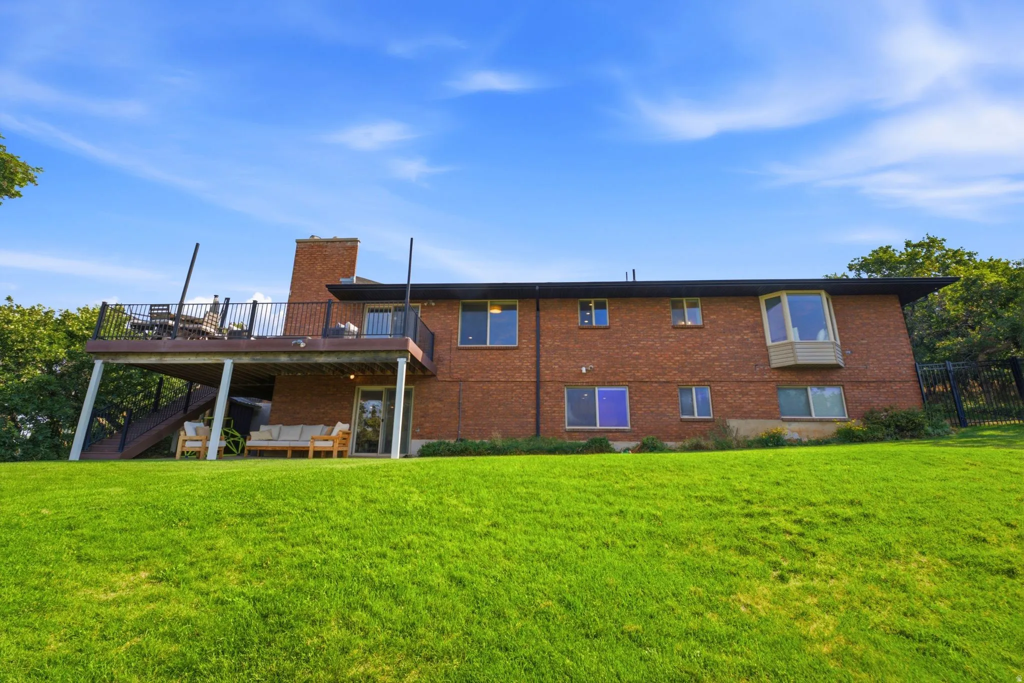 Expansive green lawn with a brick exterior featuring a multi-level deck, a prominent chimney, and a bay window
