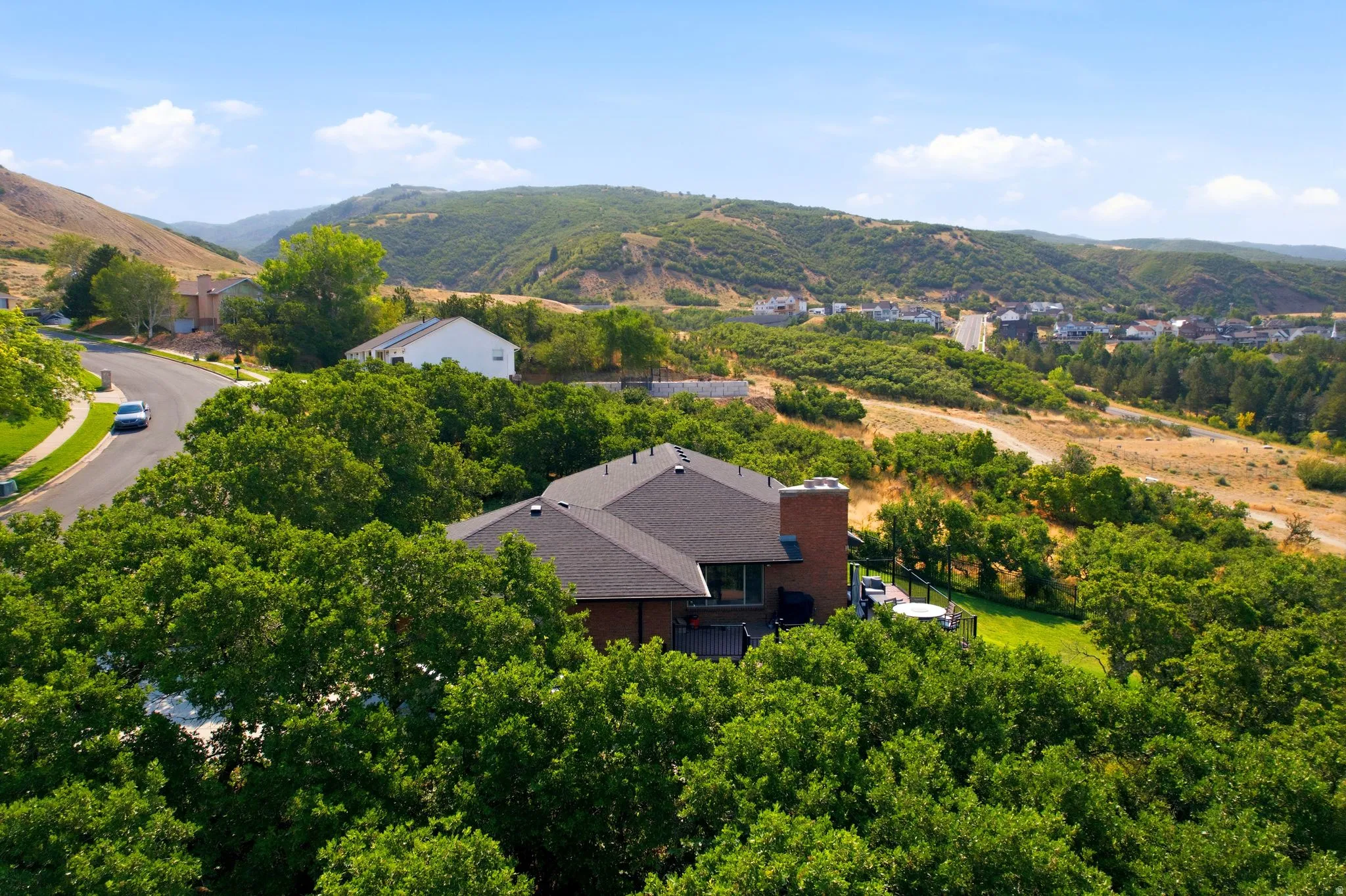 Hillside residence featuring a dark shingle roof, brick chimney, and a rear deck