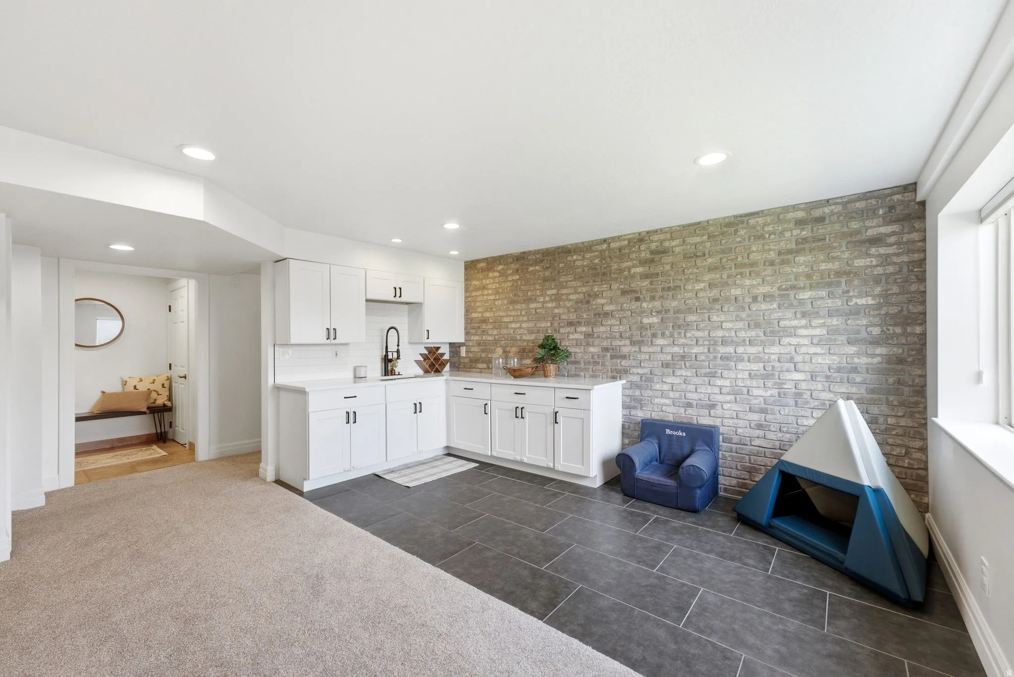 Lower level featuring a wet bar with white cabinetry and dark hardware, set against an exposed brick accent wall