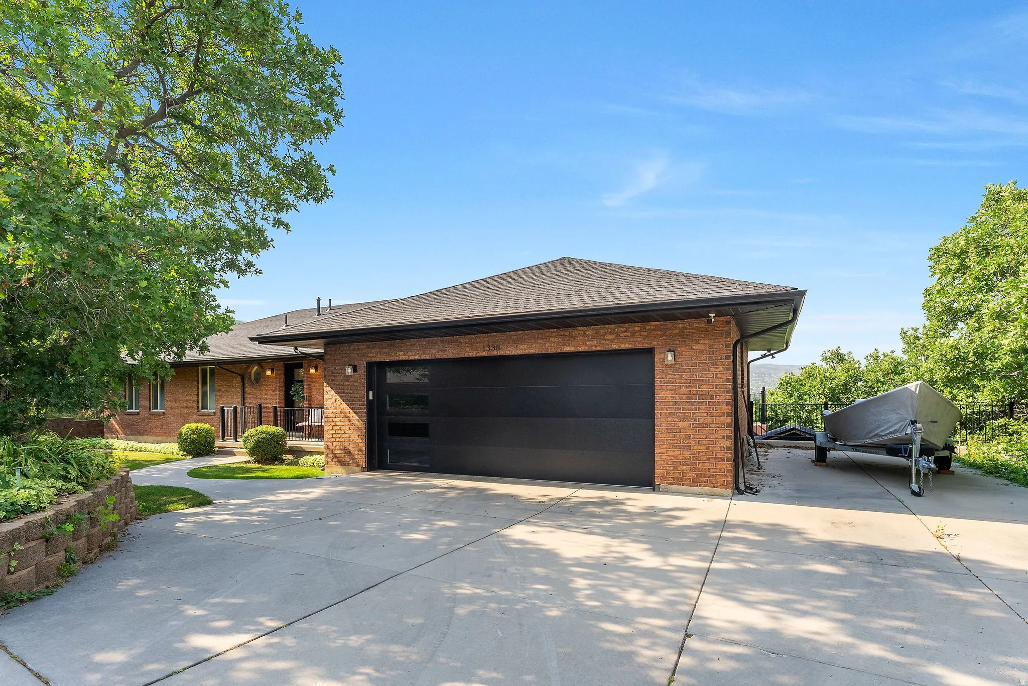 Brick exterior featuring a black garage door with frosted glass inserts, a wide concrete driveway, and mature landscaping