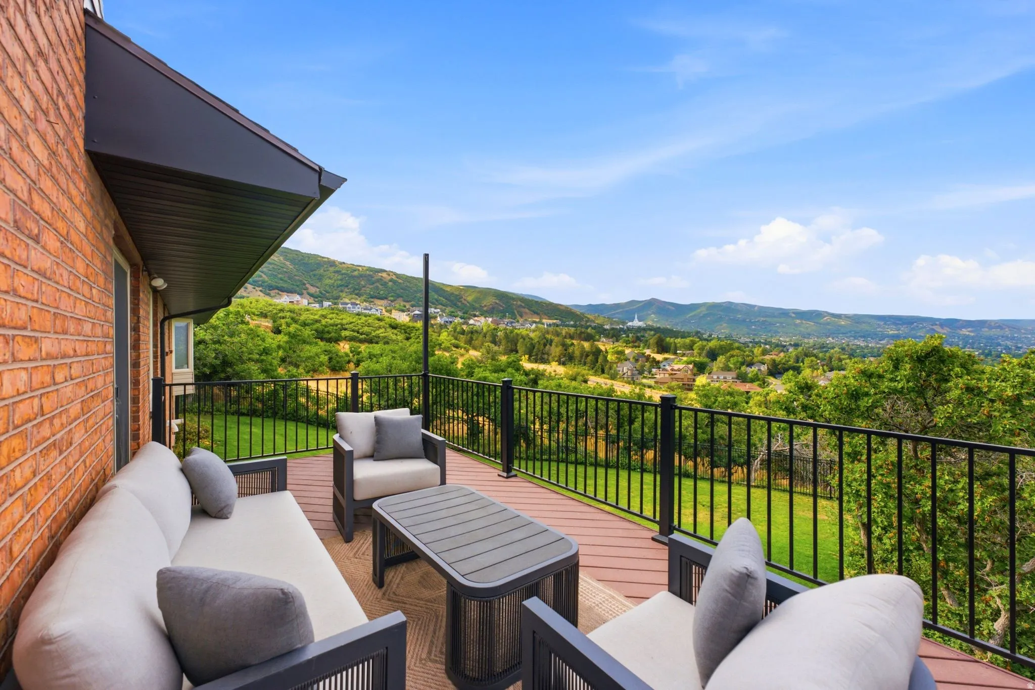 Outdoor deck featuring composite decking, black metal railing, and a brick exterior